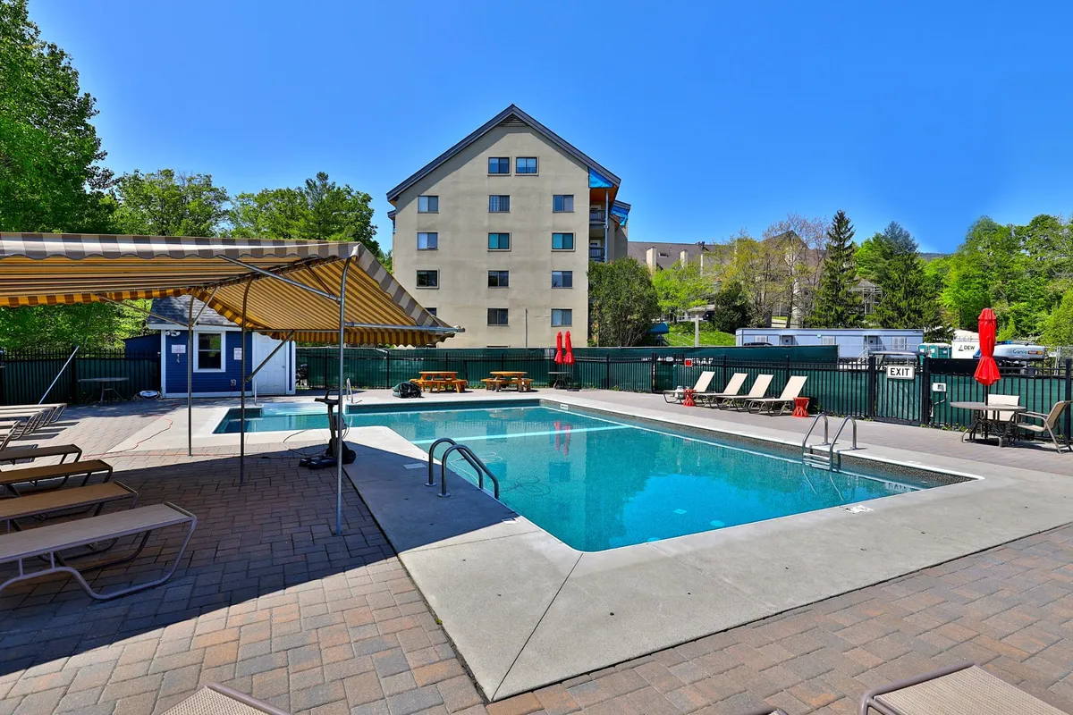 A bright, outdoor pool scene with sun loungers, umbrellas, and picnic tables, set against a summery backdrop. The vibrant mood highlights leisure and community activities ideal for warm-weather enjoyment.