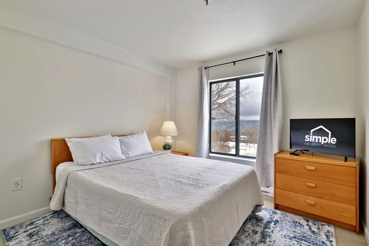 A peaceful master bedroom featuring a comfortable bed, a sunlit window with soft curtains, a dresser, and a television, all arranged to evoke relaxation and privacy. The gentle lighting and uncluttered decor create a soothing retreat perfect for unwinding after a busy day.