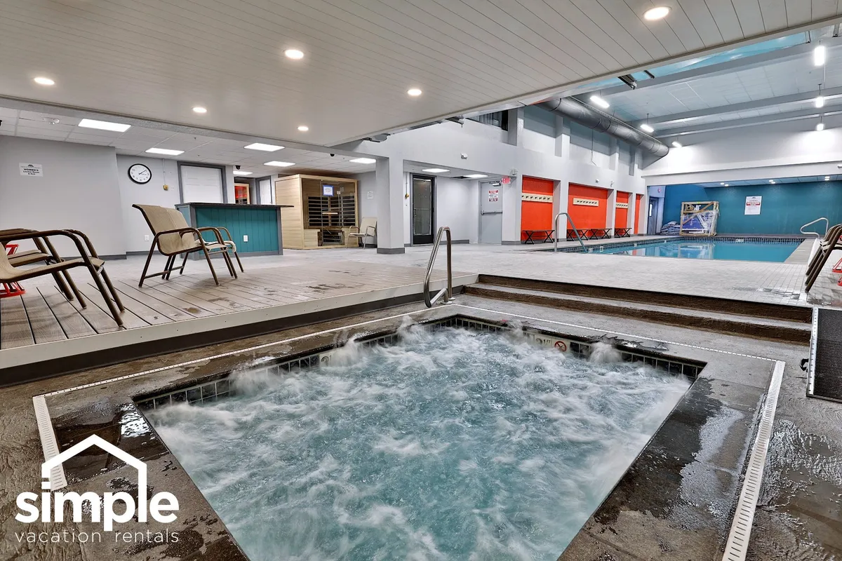 This inviting interior shot shows an indoor pool area with a hot tub, lounge chairs, and changing rooms. The ambiance blends relaxation and recreation, with guests able to unwind in the hot tub or enjoy a swim. Subtle, warm lighting and open space suggest a place for both tranquil moments and social gatherings.