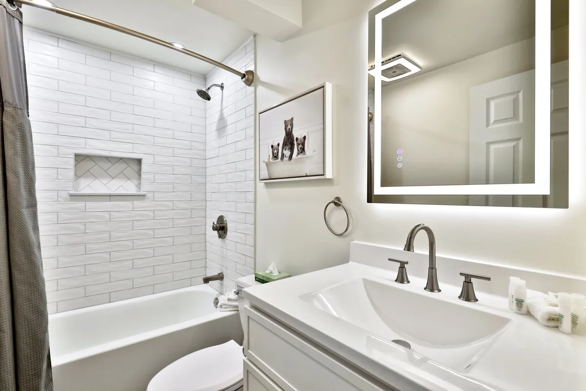 A beautifully renovated bathroom featuring a modern bathtub, elegant vanity with a mirror, soothing wall art, and soft lighting. The space is spacious and inviting, designed for both relaxation and practicality, emphasizing modern comforts and a spa-like feel.