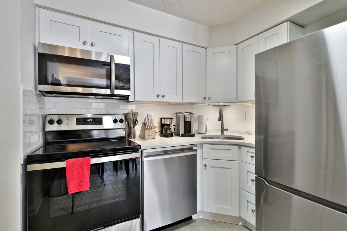 A warm, inviting kitchen space featuring stainless steel appliances, crisp white cabinetry, and a touch of color from a red kitchen towel. The layout is open and ideal for socializing or community meal preparation.