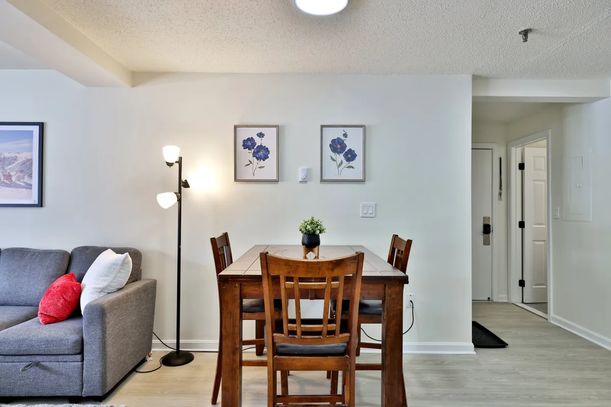 A cozy dining area with a well-set table, comfortable sofa, wall art, and a floor lamp. The space invites guests to gather for meals, game nights, or intimate conversations, blending functionality with warmth.