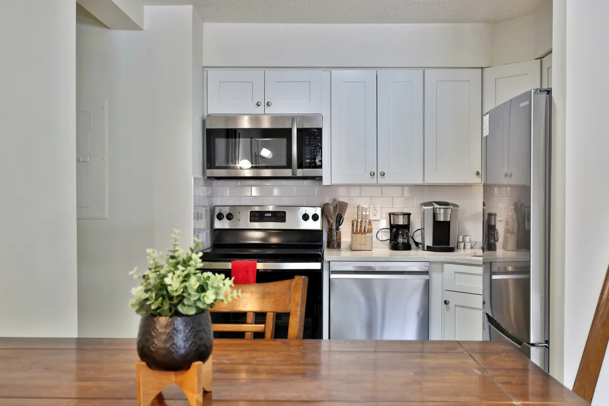 A welcoming space featuring visible kitchen appliances and a wooden dining table with a small plant centerpiece. The environment balances culinary convenience with a homey, communal feel, ideal for cooking and dining together.