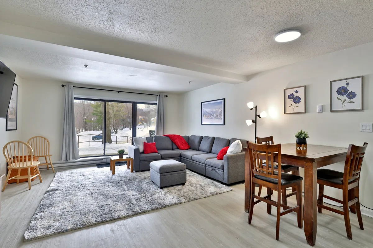 A spacious living and dining area with a large sectional sofa and a dining table set beside expansive windows offering views of the snowy outdoors. The arrangement encourages social interaction, with plenty of room for friends and family to gather after a day out.